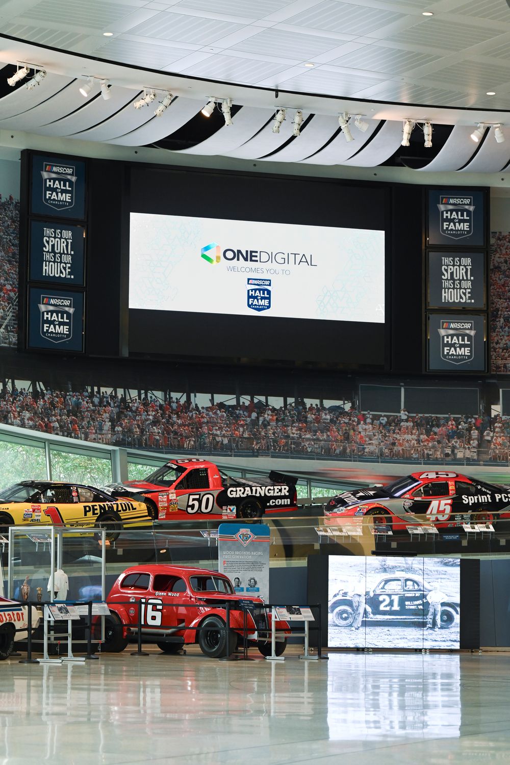 Panoramic view of a NASCAR museum display featuring multiple race cars and digital screens in a modern showroom setting.