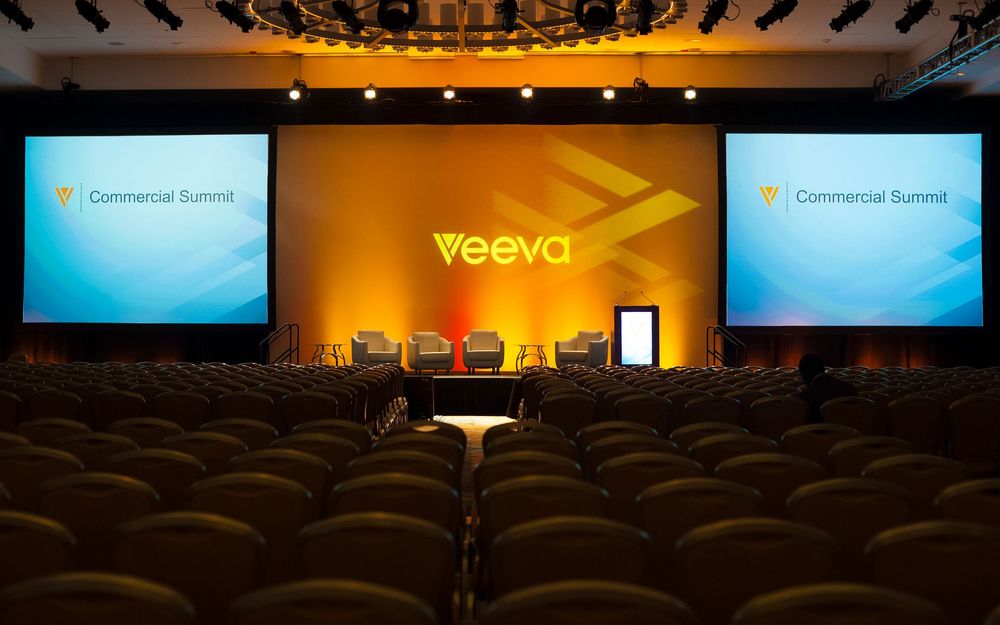 Veeva Commercial Summit conference stage with large screens and rows of empty seats in a modern auditorium.