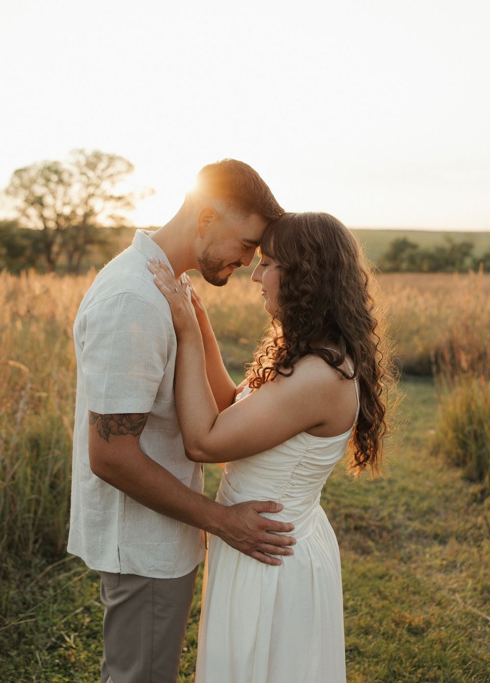 Romantic couple embraces in a golden sunlit field during sunset creating an intimate outdoor portrait session.