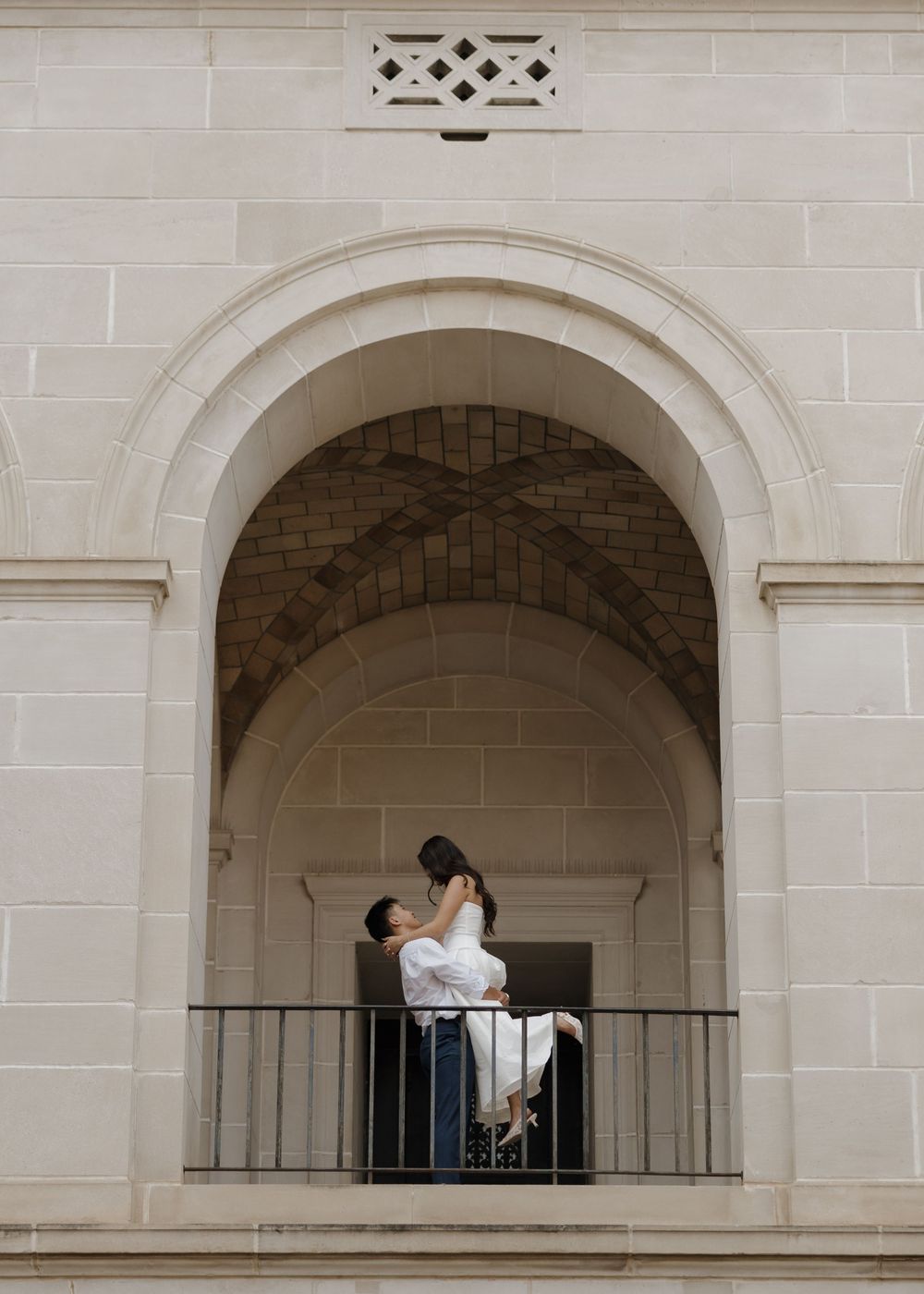 Couple embracing on an elegant stone balcony with arched architecture during a romantic engagement photo session.