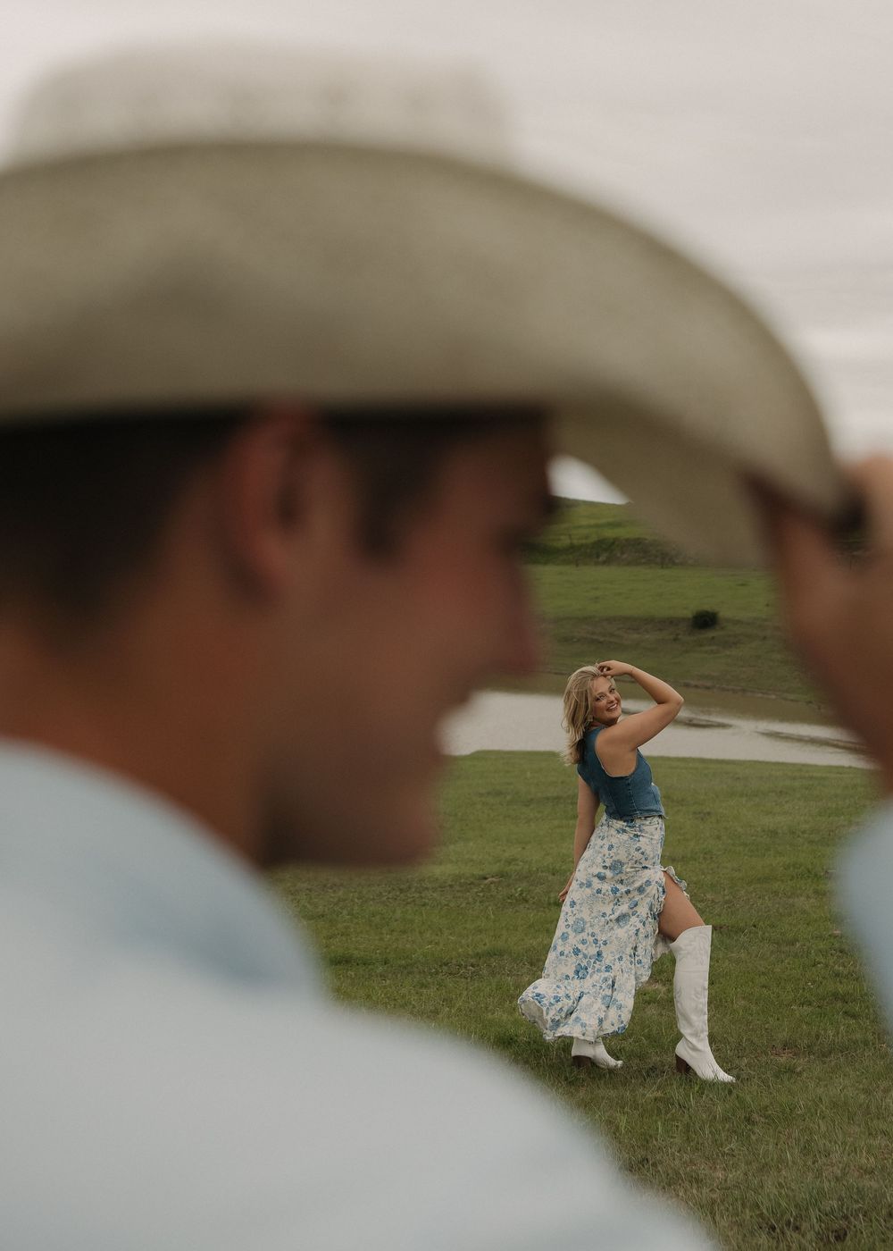 A couple in western attire dances together on a grassy field during a romantic outdoor photoshoot.