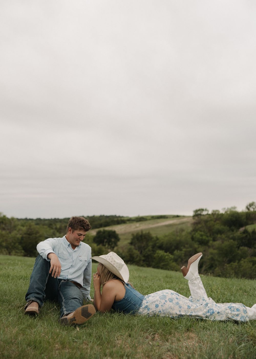 A couple lying together on a grassy hillside enjoying a peaceful moment in nature.