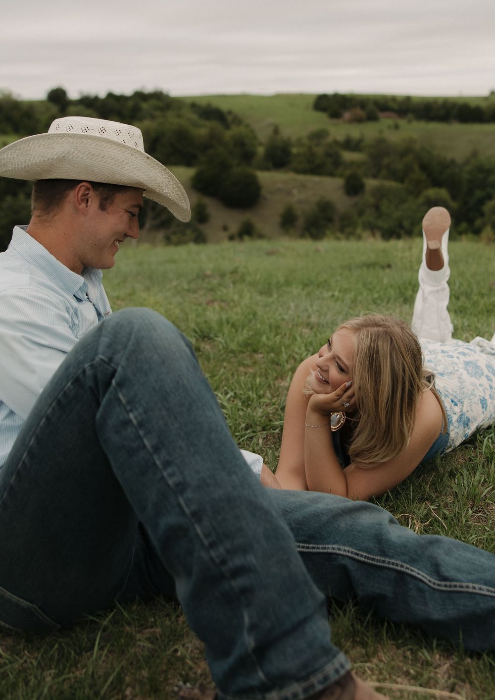 A couple relaxes together on grassy hillside during romantic countryside photoshoot.