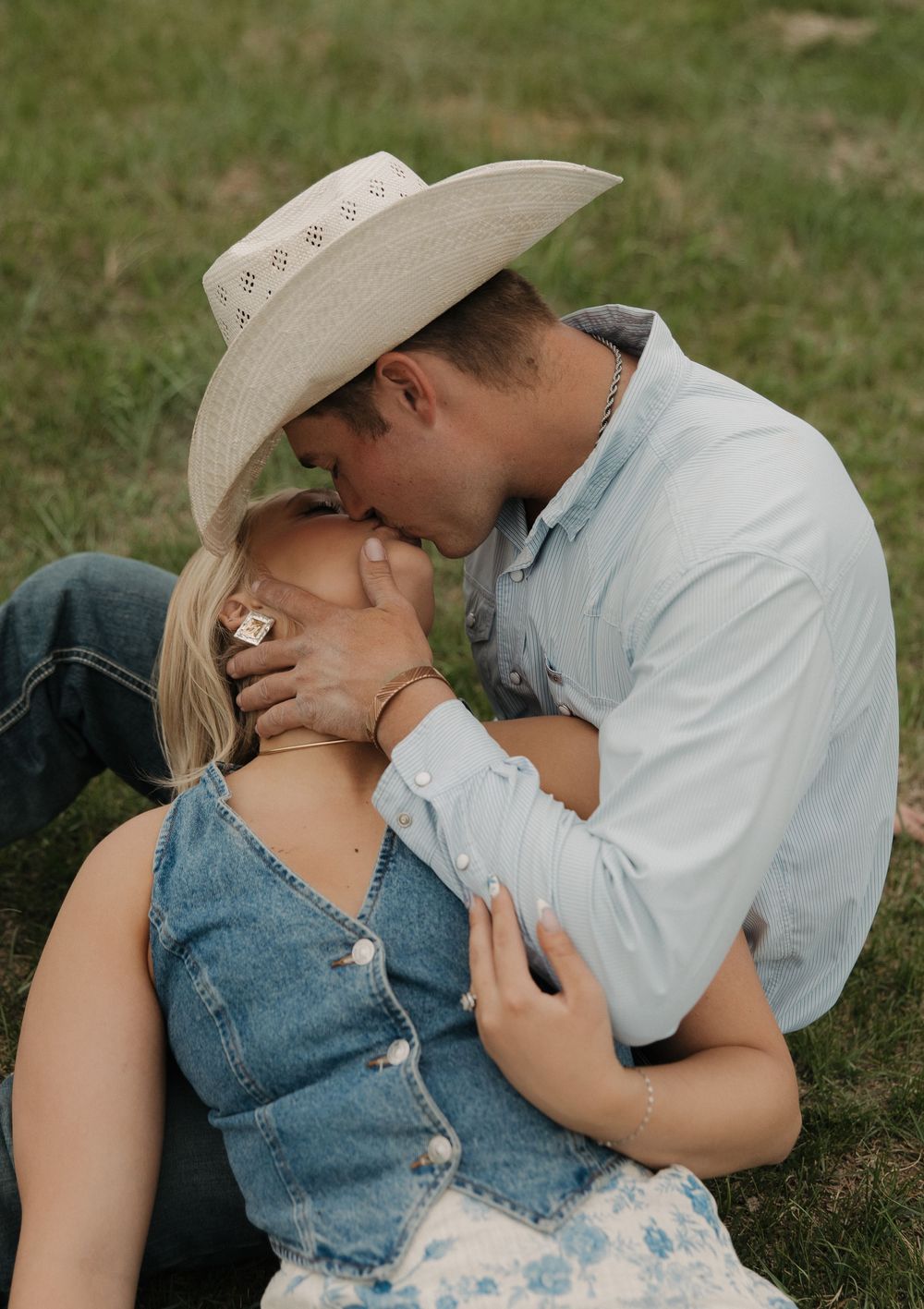 A couple embraces in a grassy meadow while wearing western attire.