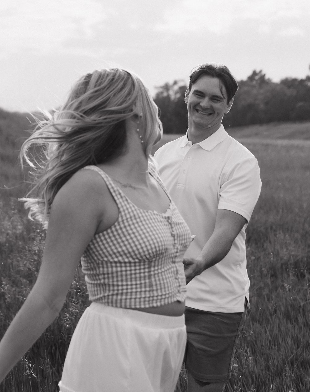 A couple in a field shares a romantic moment in black and white as they dance together.