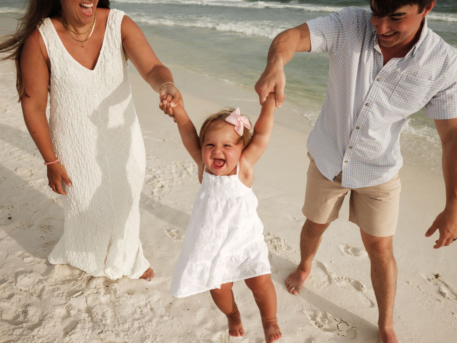 Family in white clothing walking and playing on beach sand.