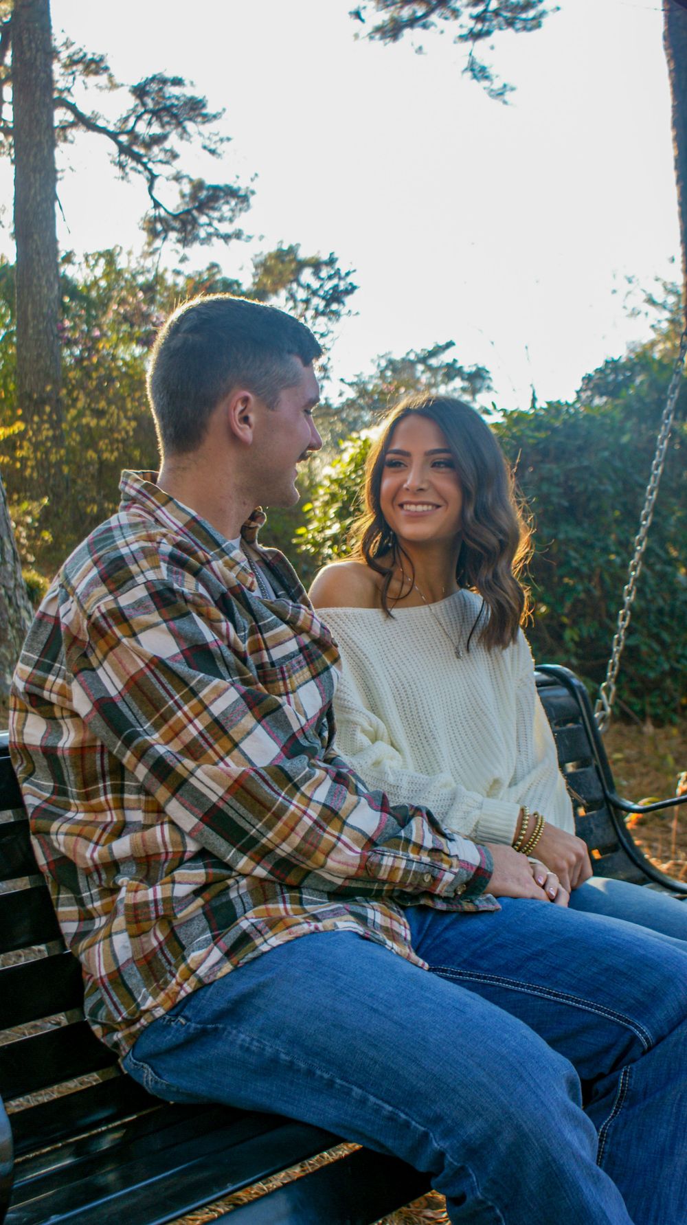A couple sits close together on a wooden bench swing during their engagement photoshoot.