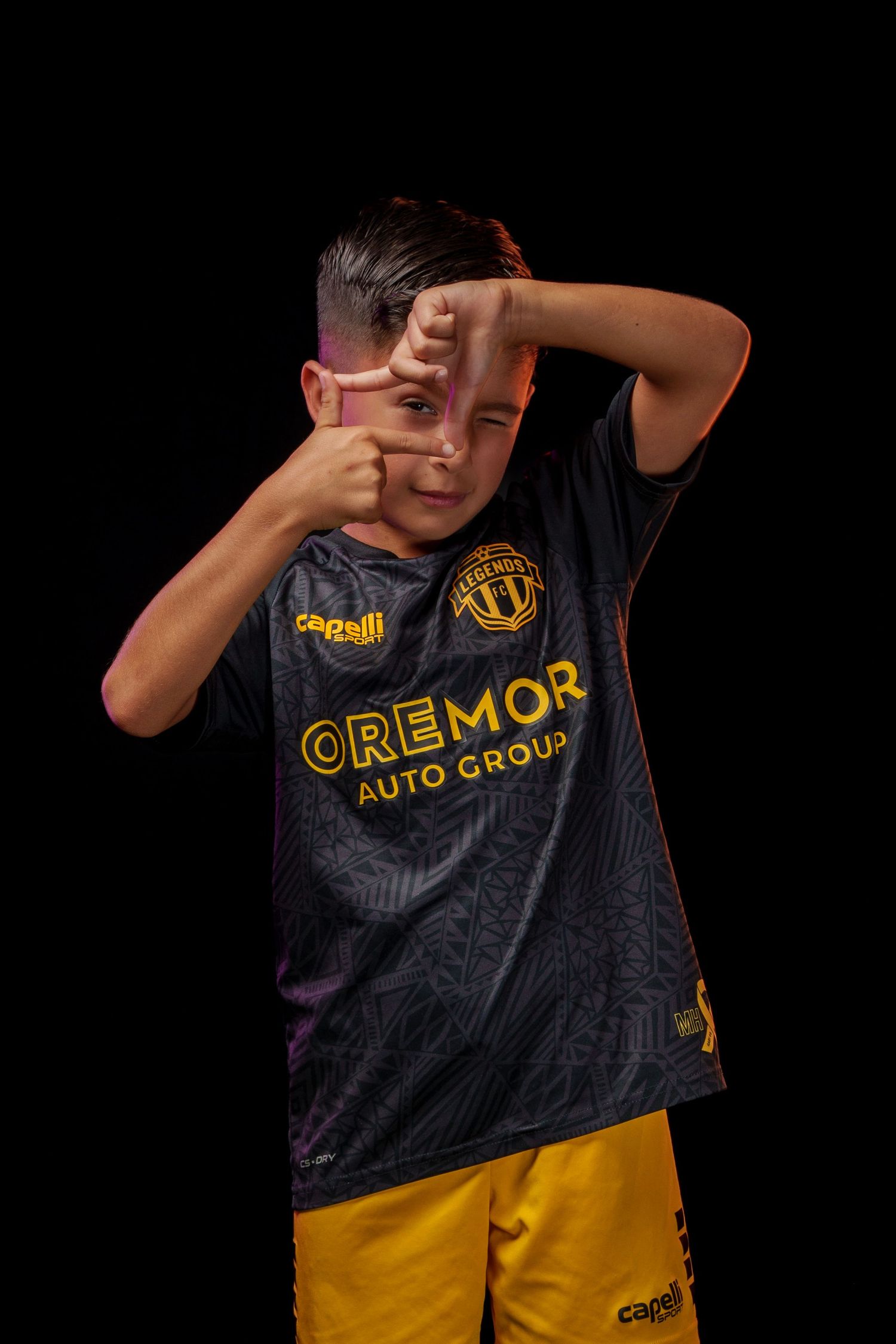 Person in black and yellow Legends FC jersey making a dramatic pose against dark background.