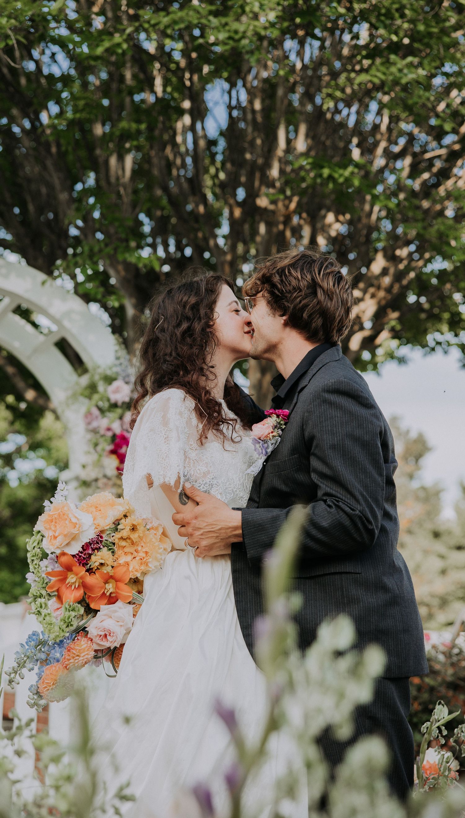 A couple stands on a misty forest path with rustic wooden railings, the bride wearing an elegant lace wedding dress.