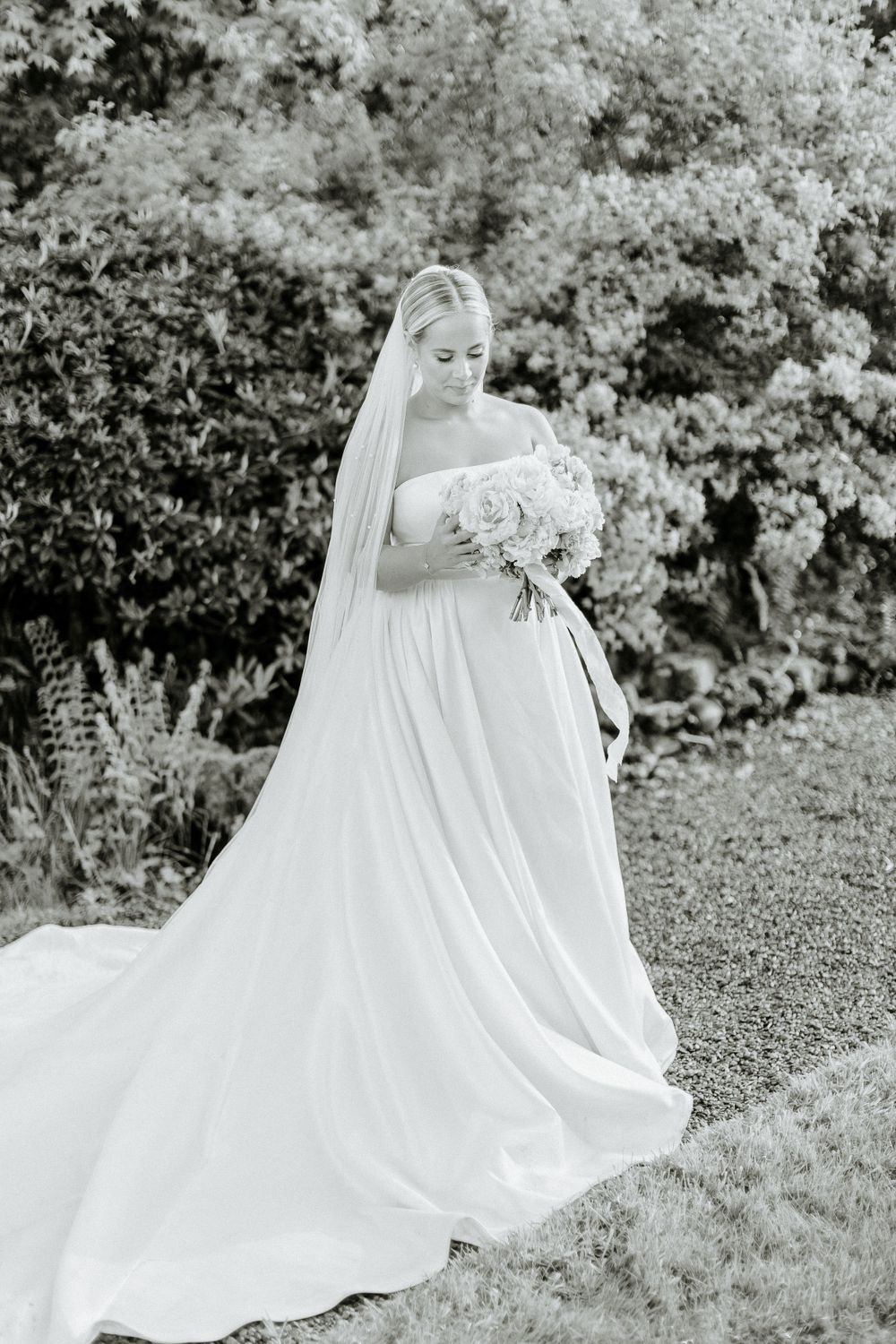 Dramatic black and white bridal portrait with flowing veil and garden backdrop.