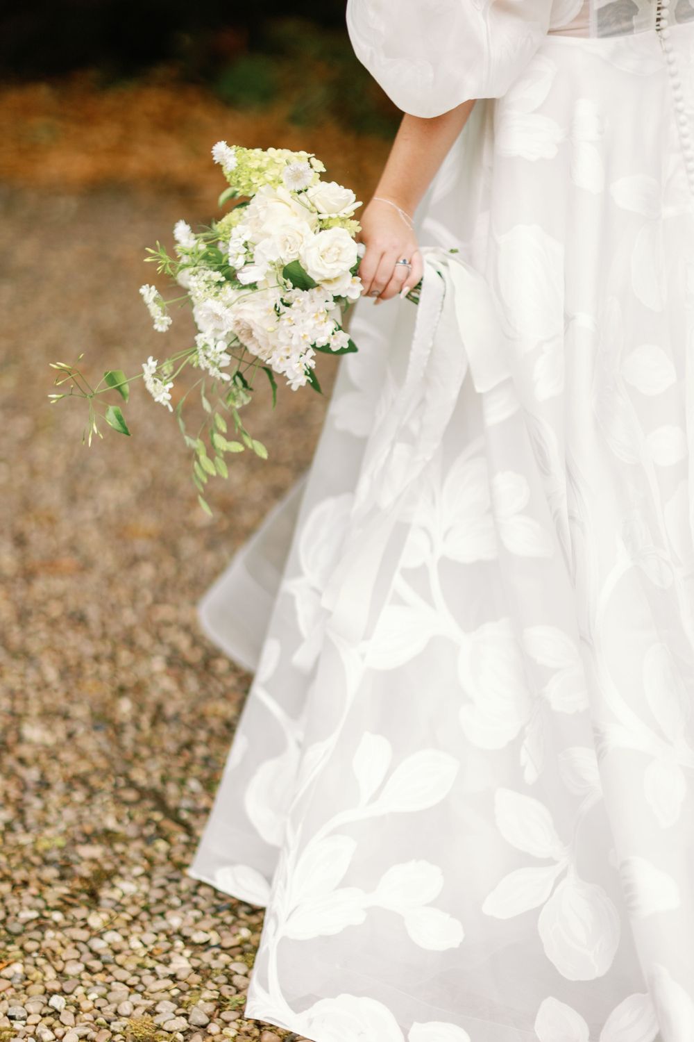 Detail shot of white wedding dress and cascading bouquet against gravel path.