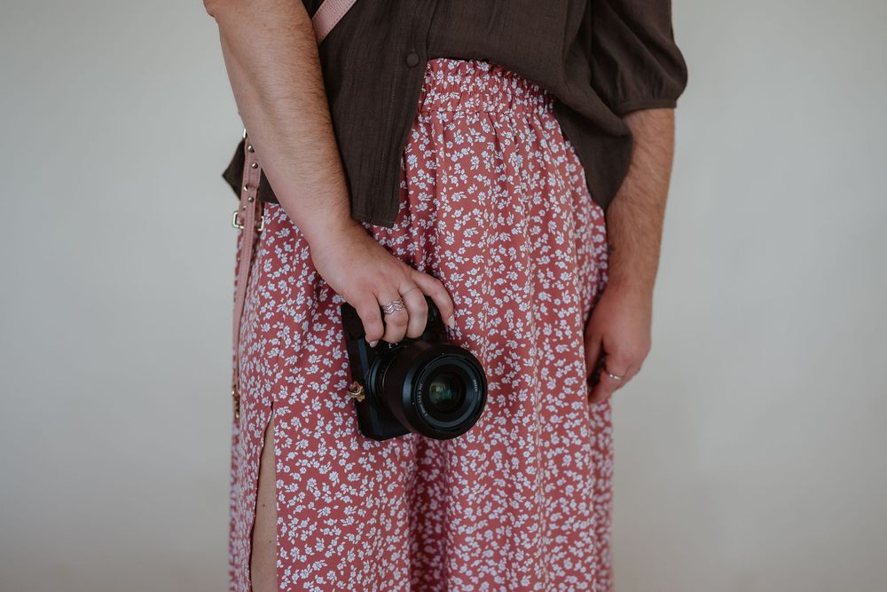 Woman in pink floral dress holding a camera in various poses against a light background.