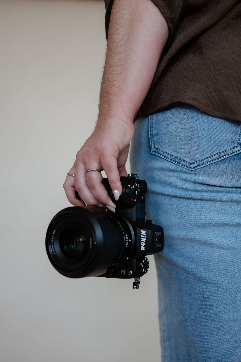 Close-up of hands holding professional camera with lens against light background.
