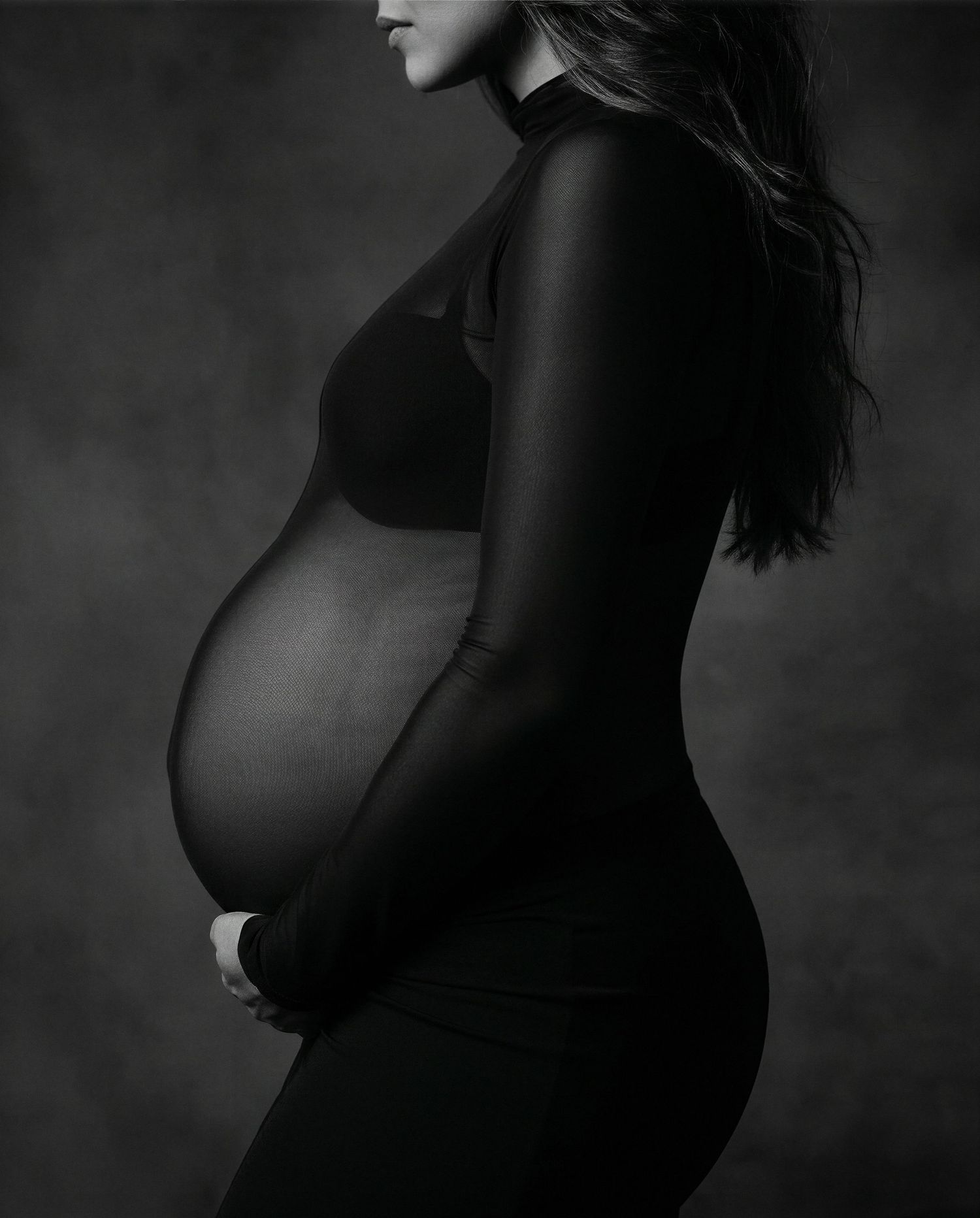 Black and white maternity photo of pregnant woman in profile cradling baby bump wearing a black turtleneck.