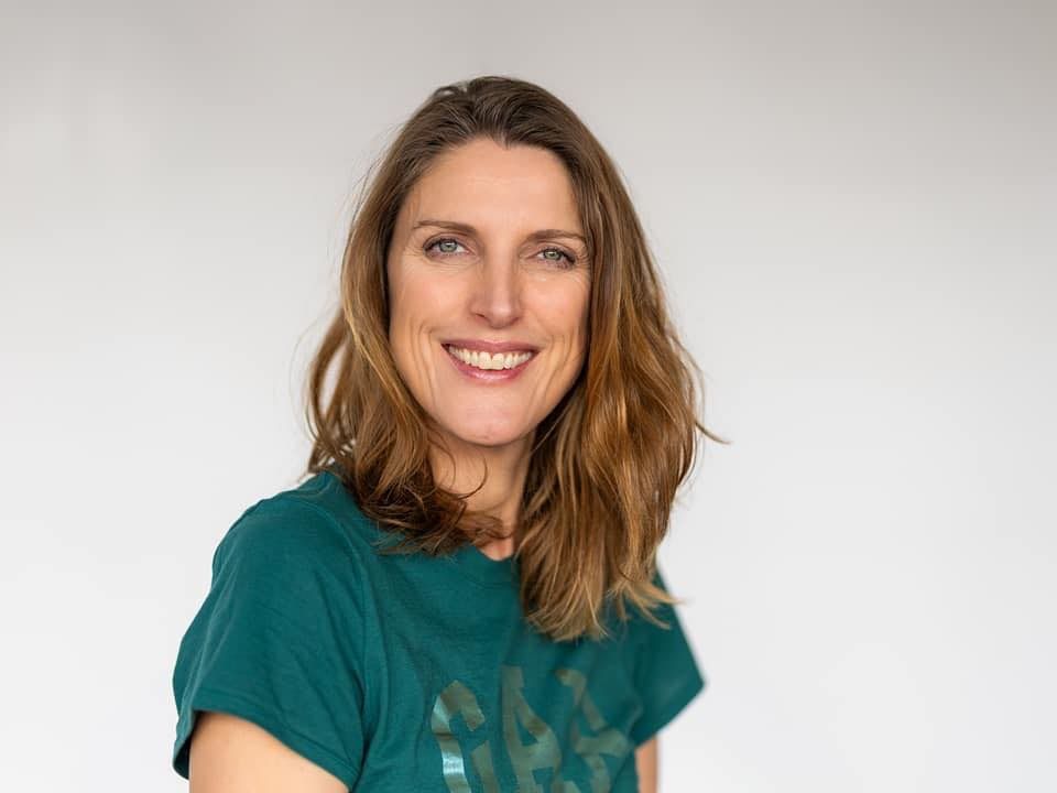 Professional headshot of someone wearing a dark green t-shirt against a light gray background.