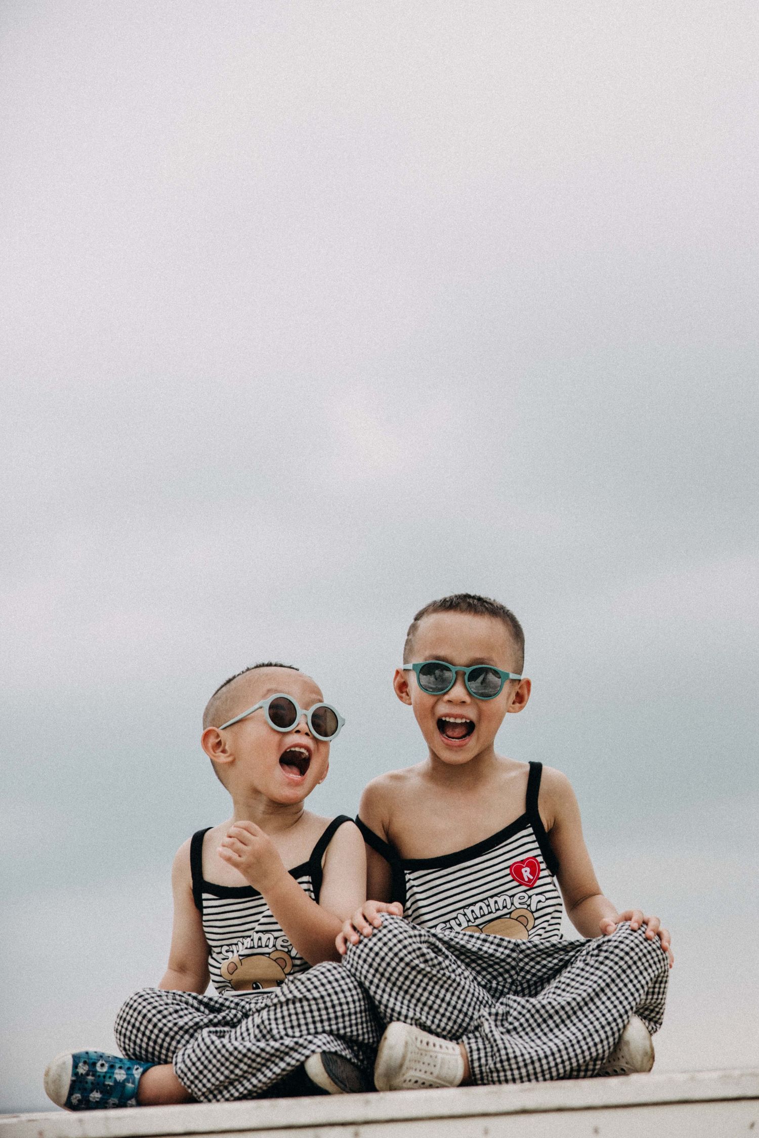 Two children in matching striped outfits sitting and laughing together against a cloudy sky.