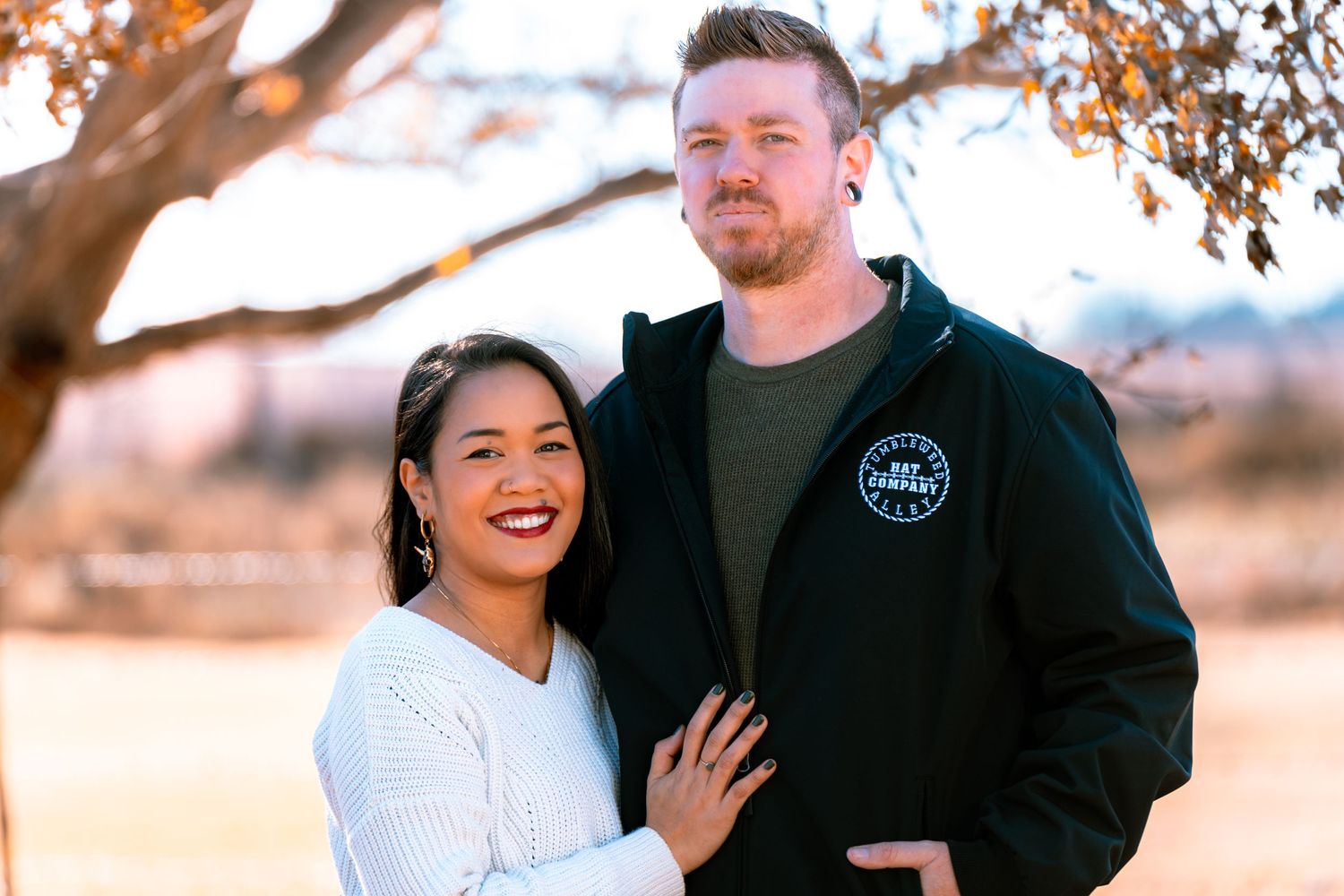 A couple embraces outdoors during golden hour with autumn trees in the background.