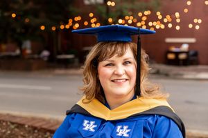 Woman smiling in University of Kentucky blue and gold graduation cap and gown outdoors.