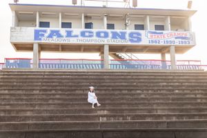 A person in white dress walks down concrete stadium bleachers during golden hour.