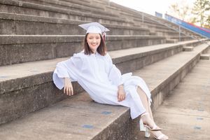 Graduate in white cap and gown sitting on concrete steps in a collage of graduation photo poses.