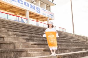 Figure in white dress descends large concrete stadium steps with bright sunlight.