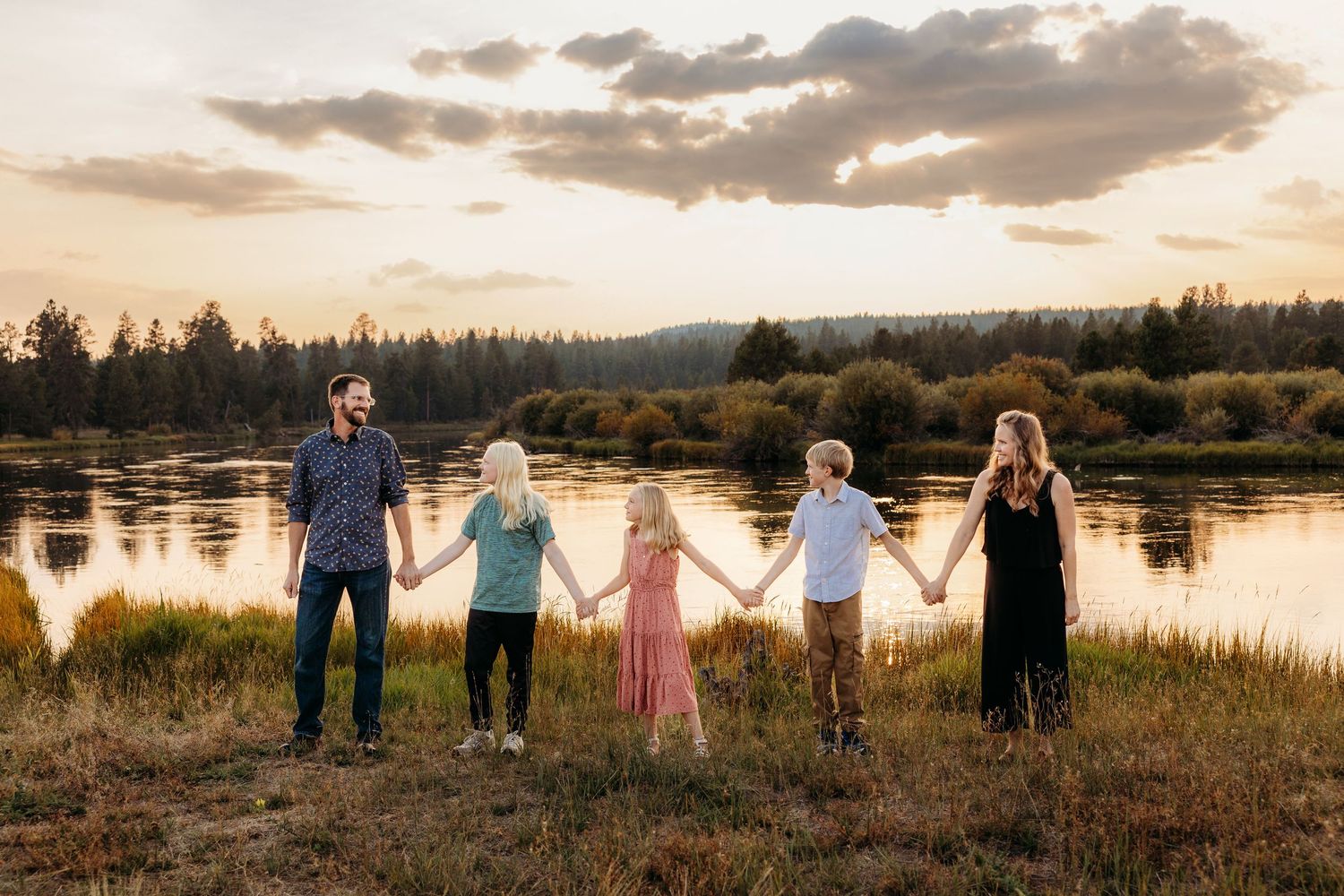 Family portrait on wooden bridge with mountains in background during sunset.