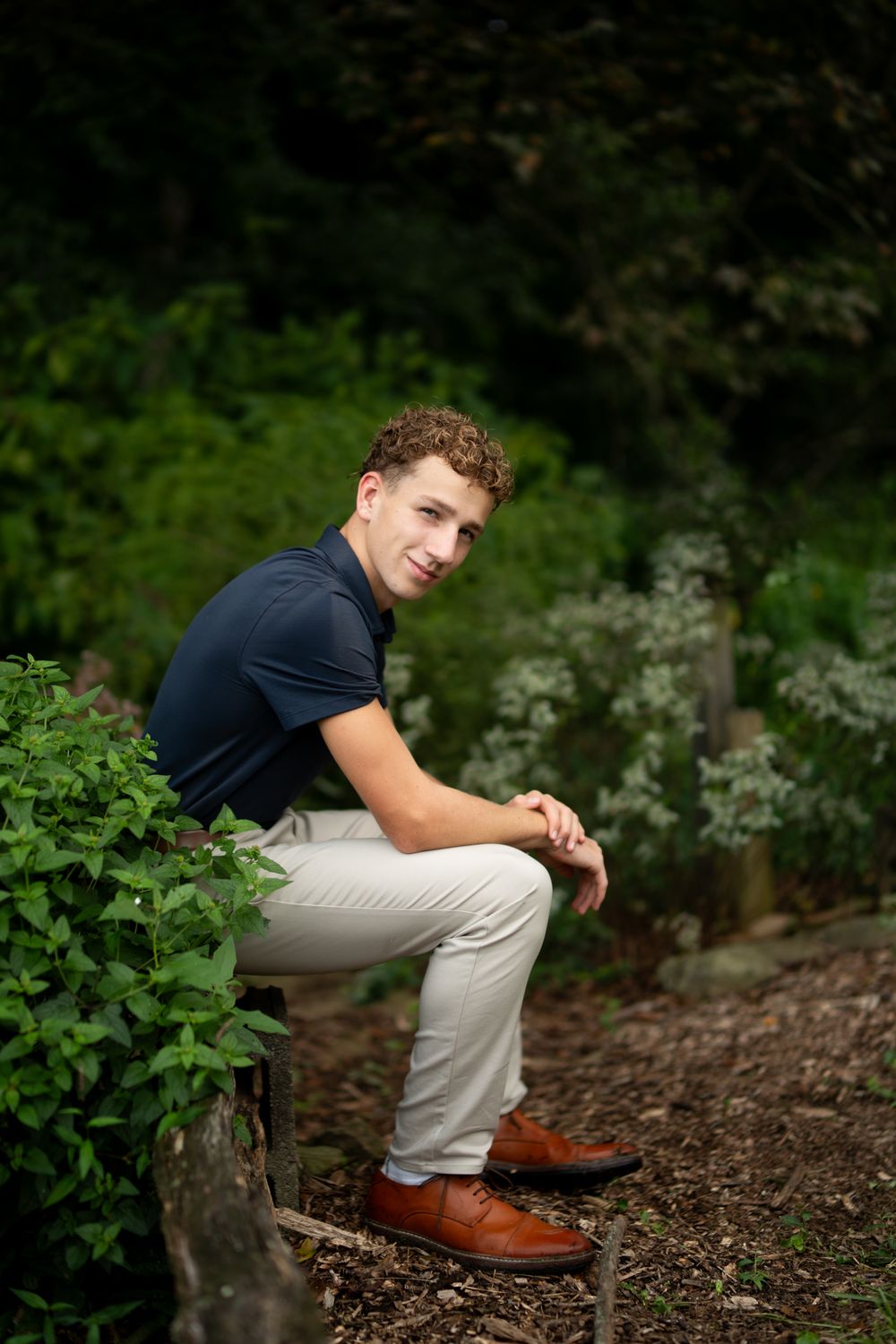 Teen male sitting on a log in a garden