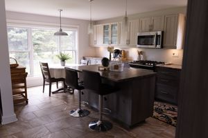 Modern kitchen with dark island, white cabinets and dining nook with large windows.