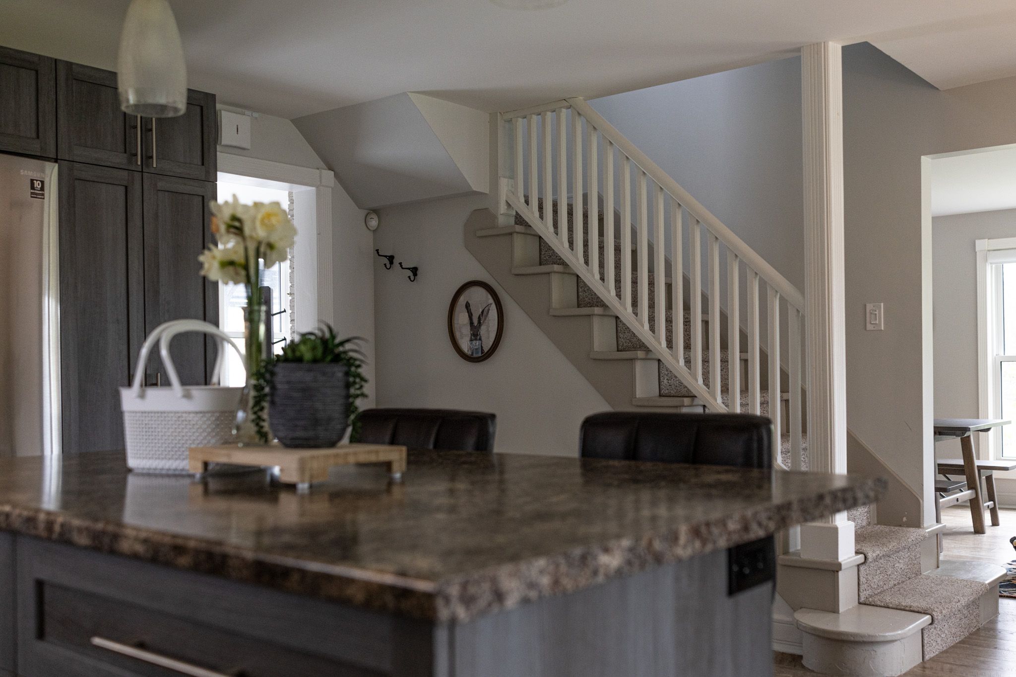 Elegant kitchen featuring marble countertops, dark cabinets and white staircase railings.