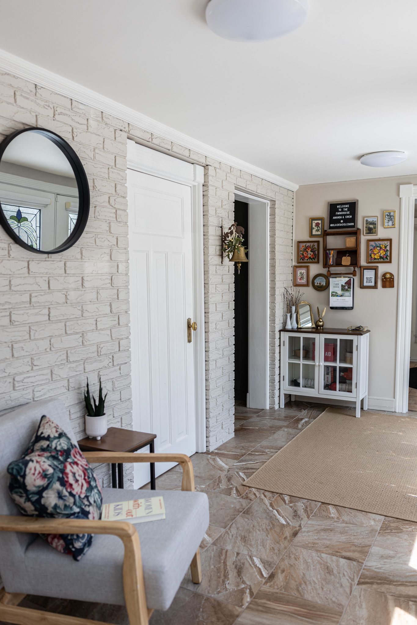 Modern entryway with white brick wall, round mirror, gray armchair, and gallery wall decor.