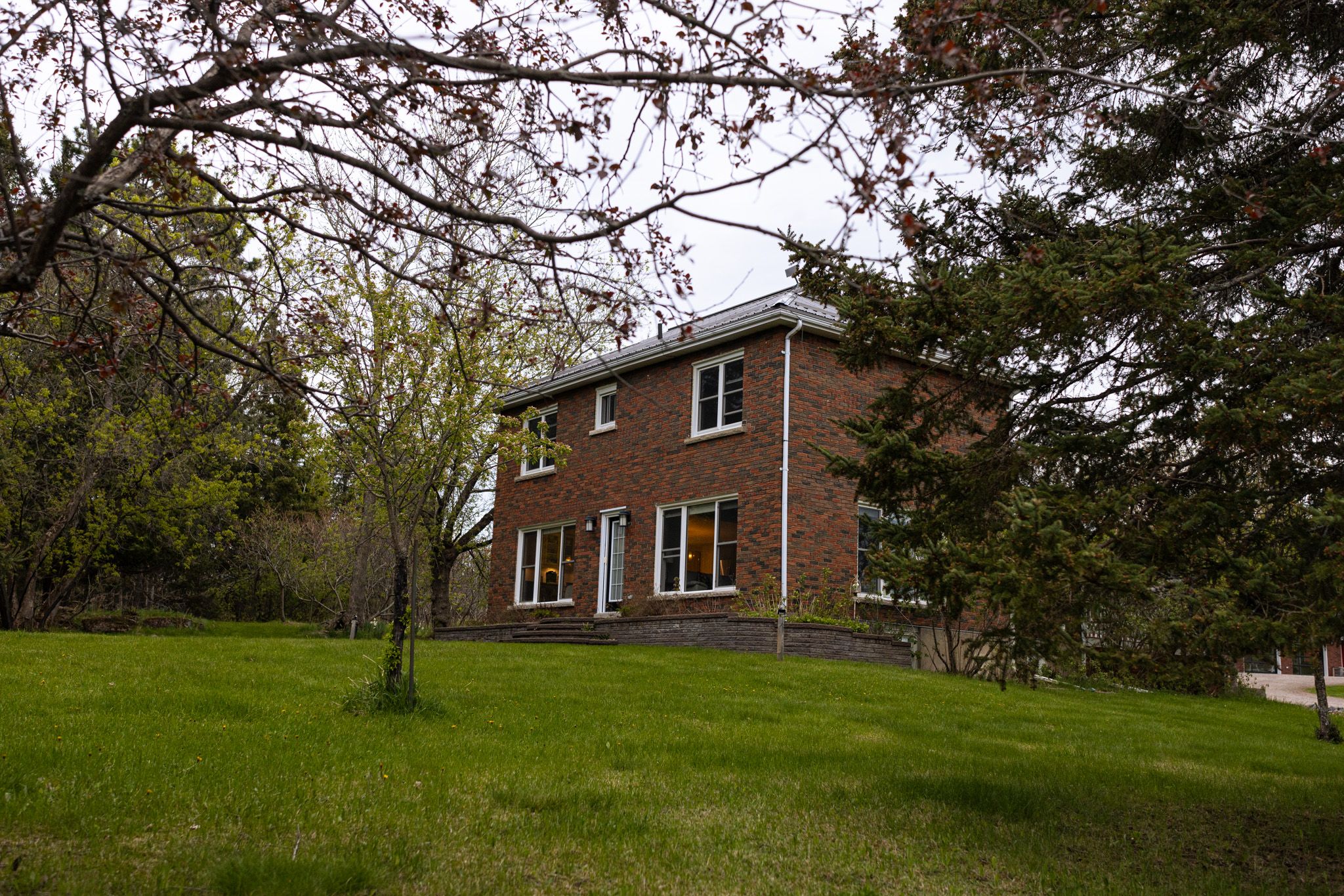 Two-story brick house with green lawn and trees in springtime.