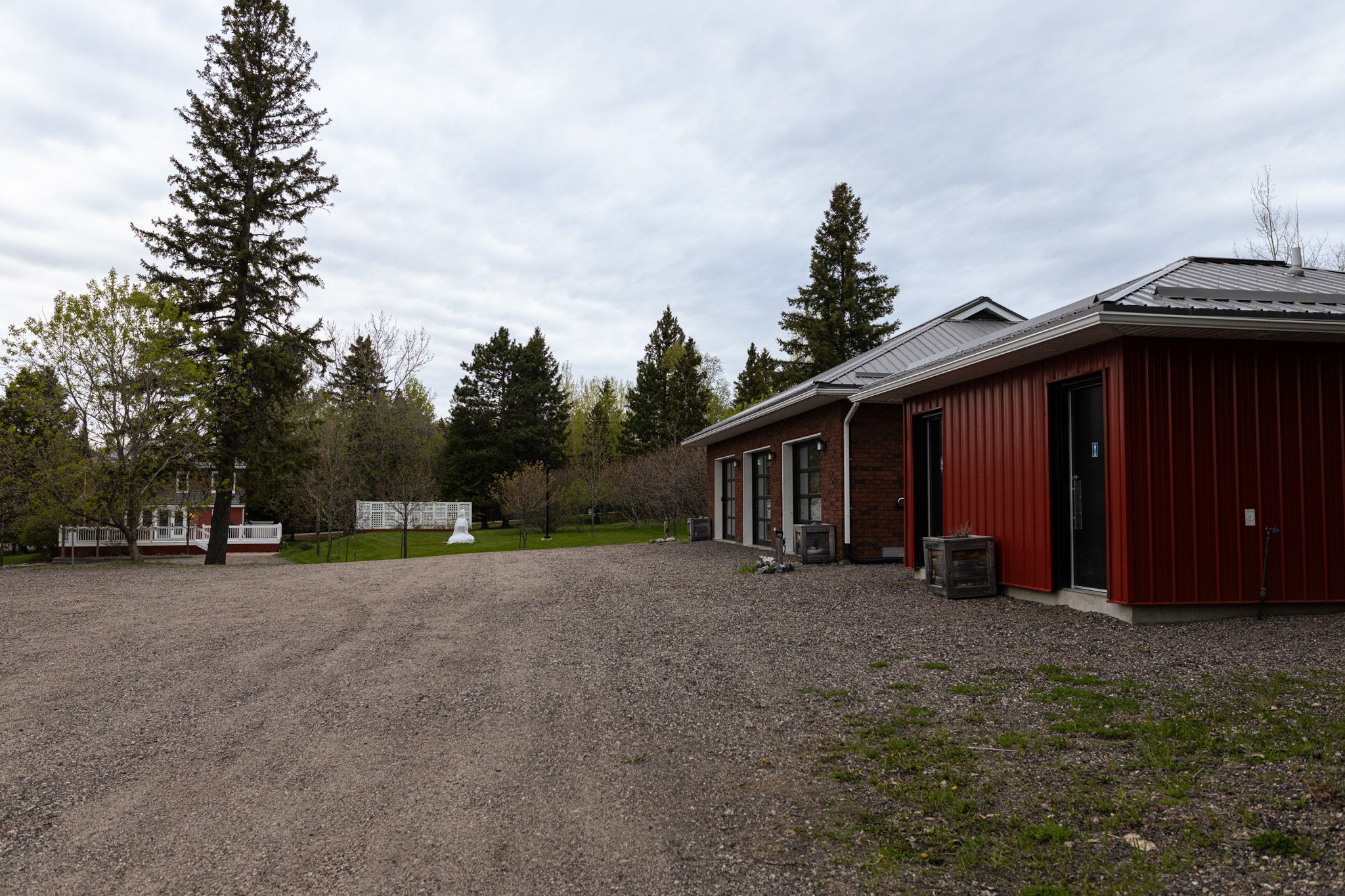 Long red building with gravel parking area surrounded by evergreen trees.
