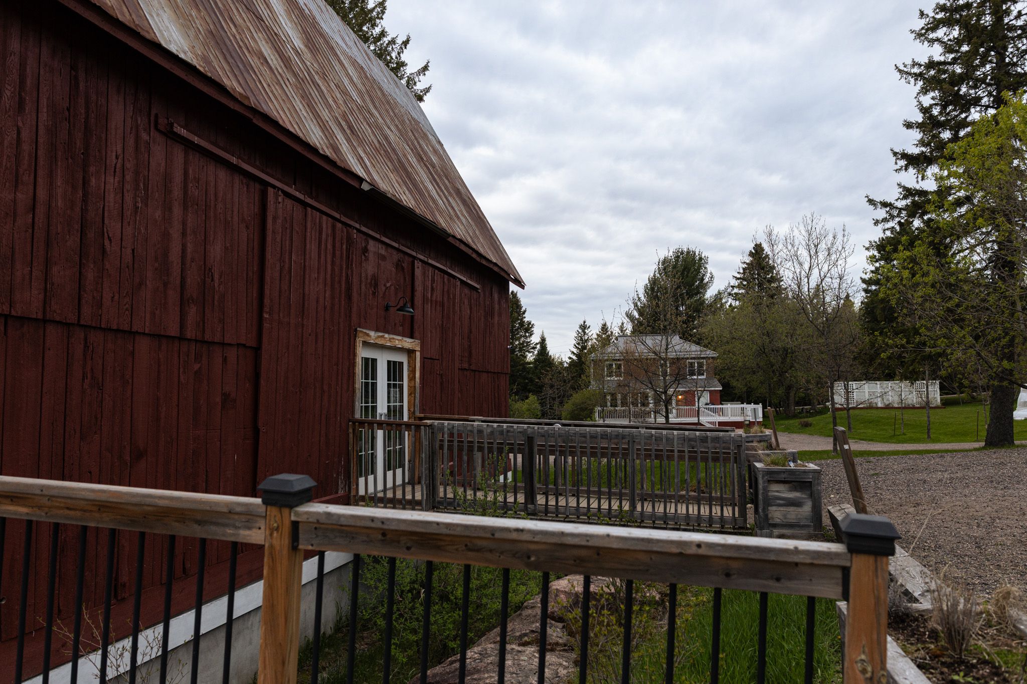 Rustic brown barn with wooden deck and railing under cloudy sky.
