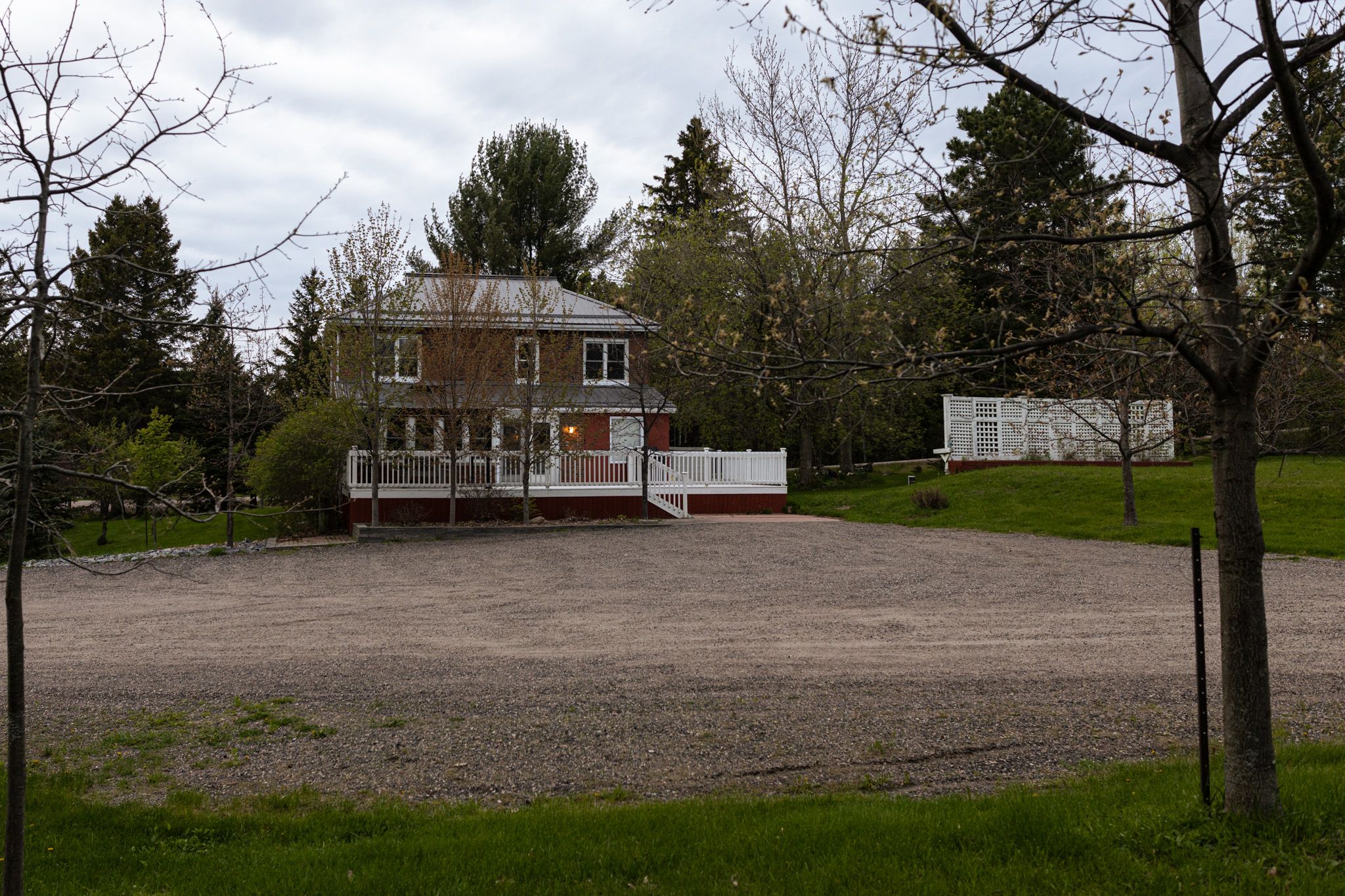 Two-story building with front porch and large gravel parking area surrounded by trees.