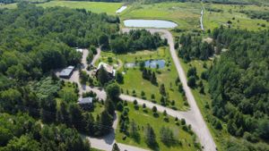 Aerial view of a winding road through green countryside with scattered buildings and ponds surrounded by forest.
