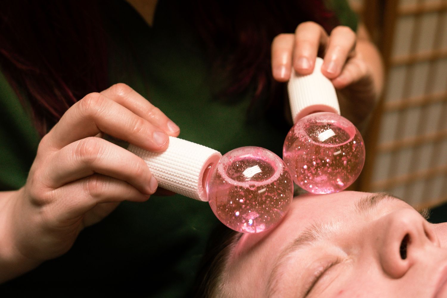Person receiving facial treatment with pink clay mask being applied.