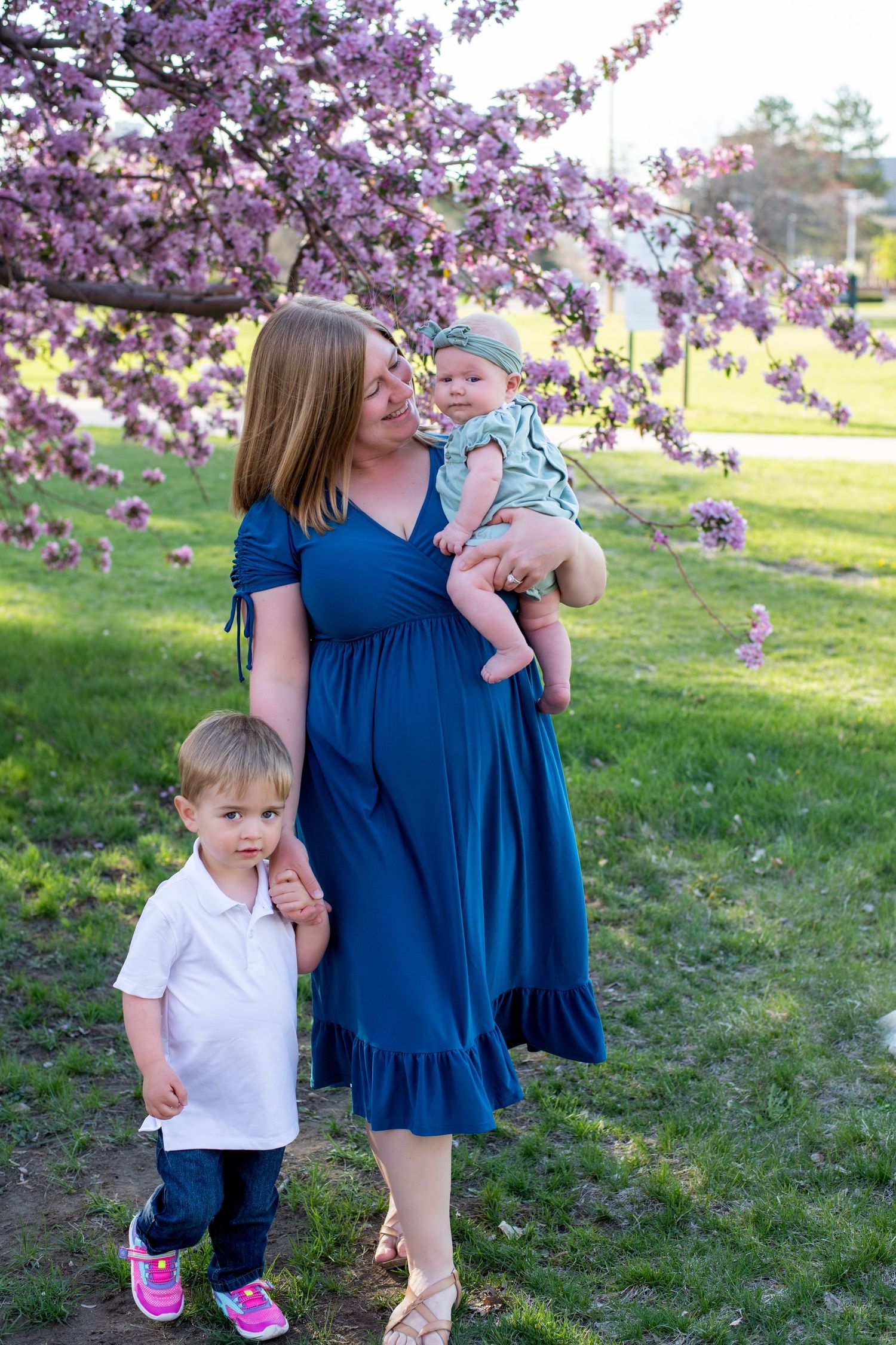 A springtime portrait under blooming cherry blossoms featuring a blue dress against pink flowers.