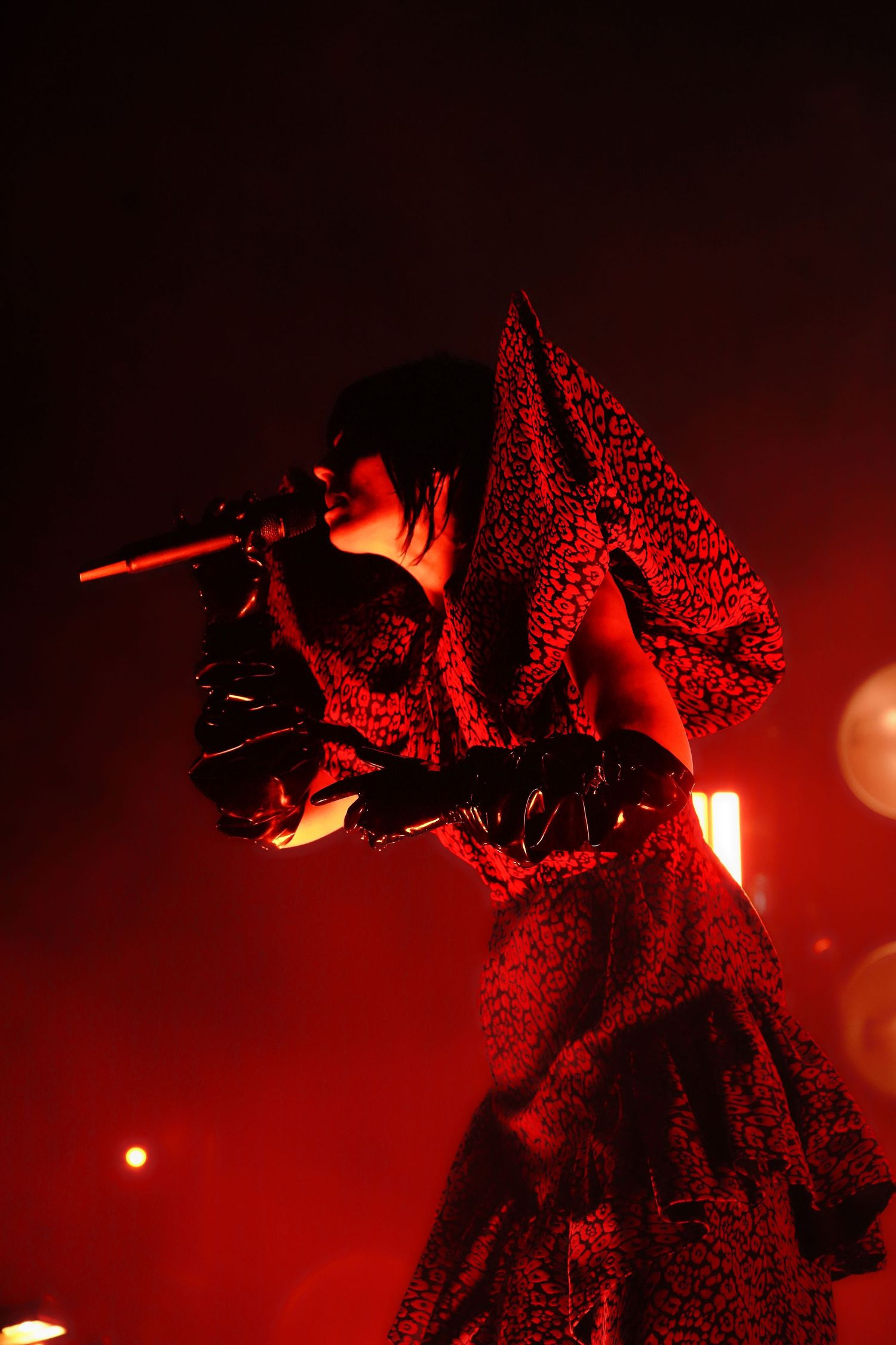 Silhouetted performer in dramatic red lighting creates dynamic shapes during an energetic stage performance.