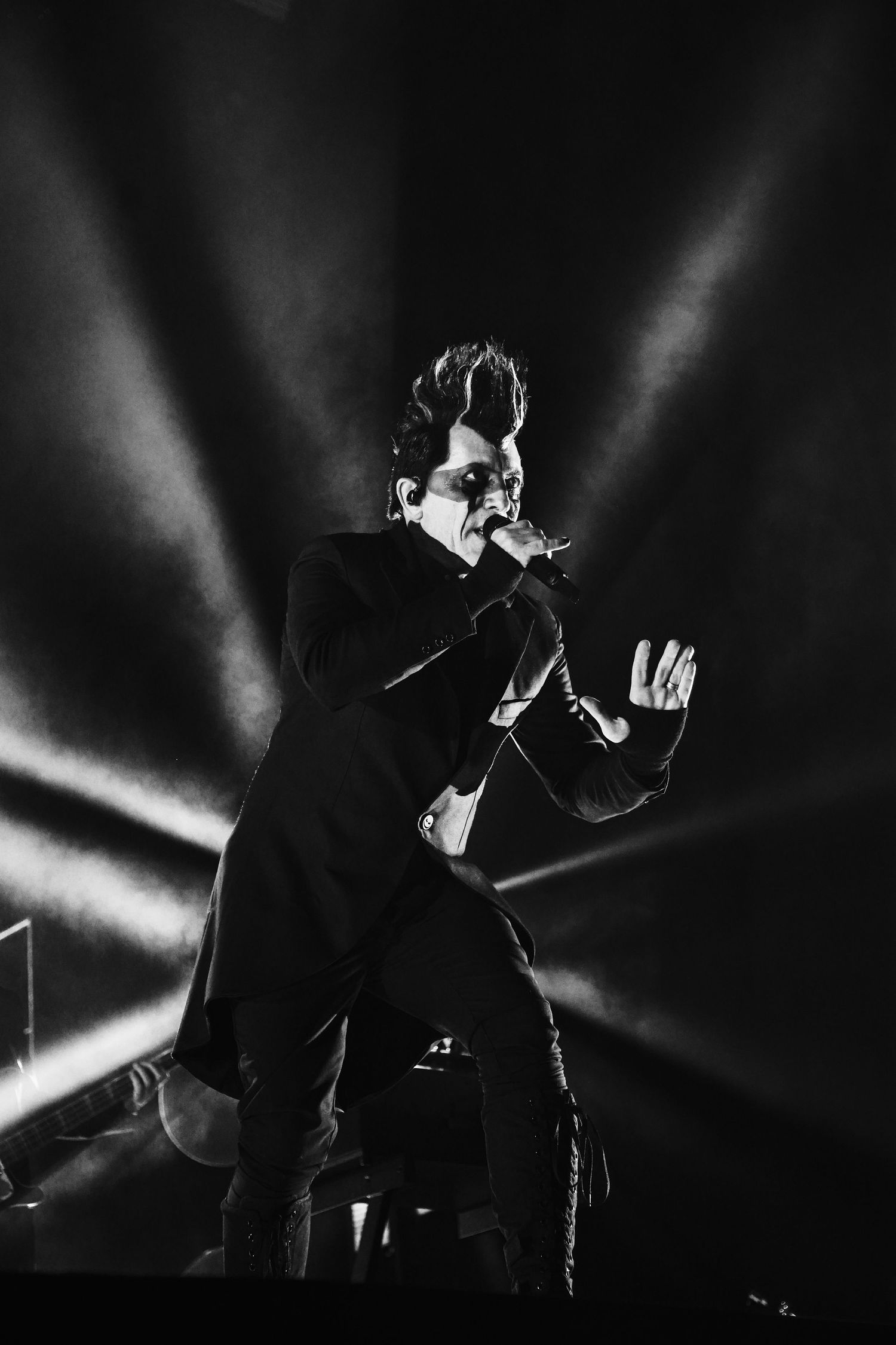 A performer in a black suit silhouetted against dramatic beams of light on stage during a concert performance.