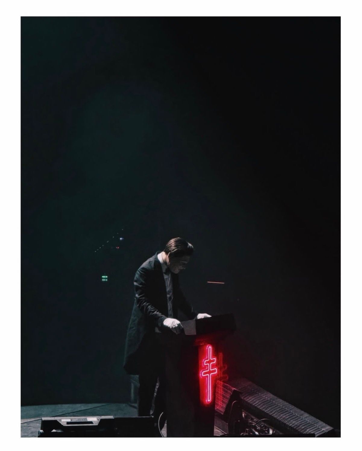 A performer in a dark suit stands on stage illuminated by dramatic red and blue lighting effects during a show.
