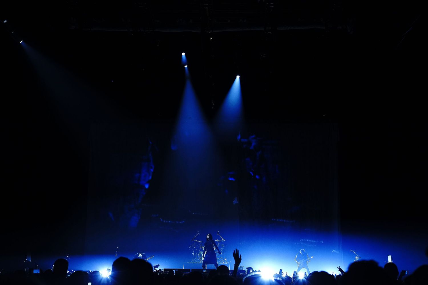 A rock band performs on a dramatic stage bathed in blue and white spotlights during a live concert.
