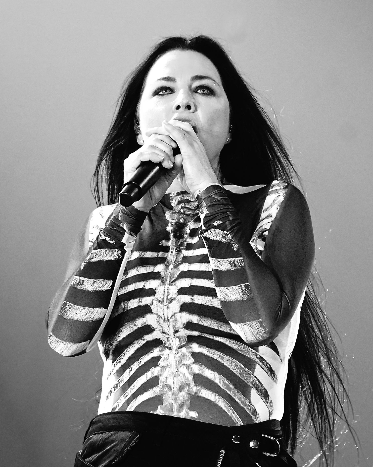 Woman singer performing on stage in black and white, wearing skeleton costume top, holding microphone with long dark hair.