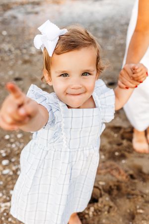 A little girl points at the camera during a beach session in the fall on the coast of Connecticut