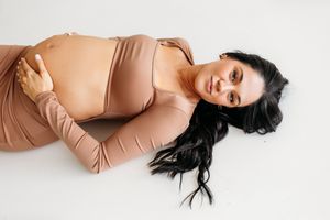 A pregnant mother in tan holds her belly during a studio session in Connecticut