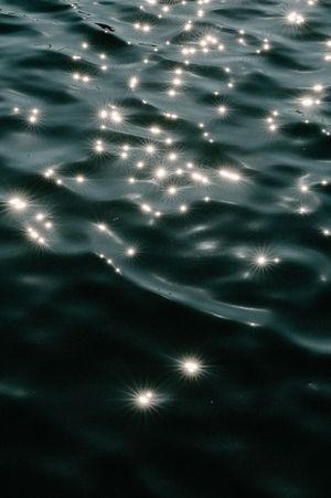 Sparkling sunlight reflections dancing on dark ocean water creating a magical starry pattern.