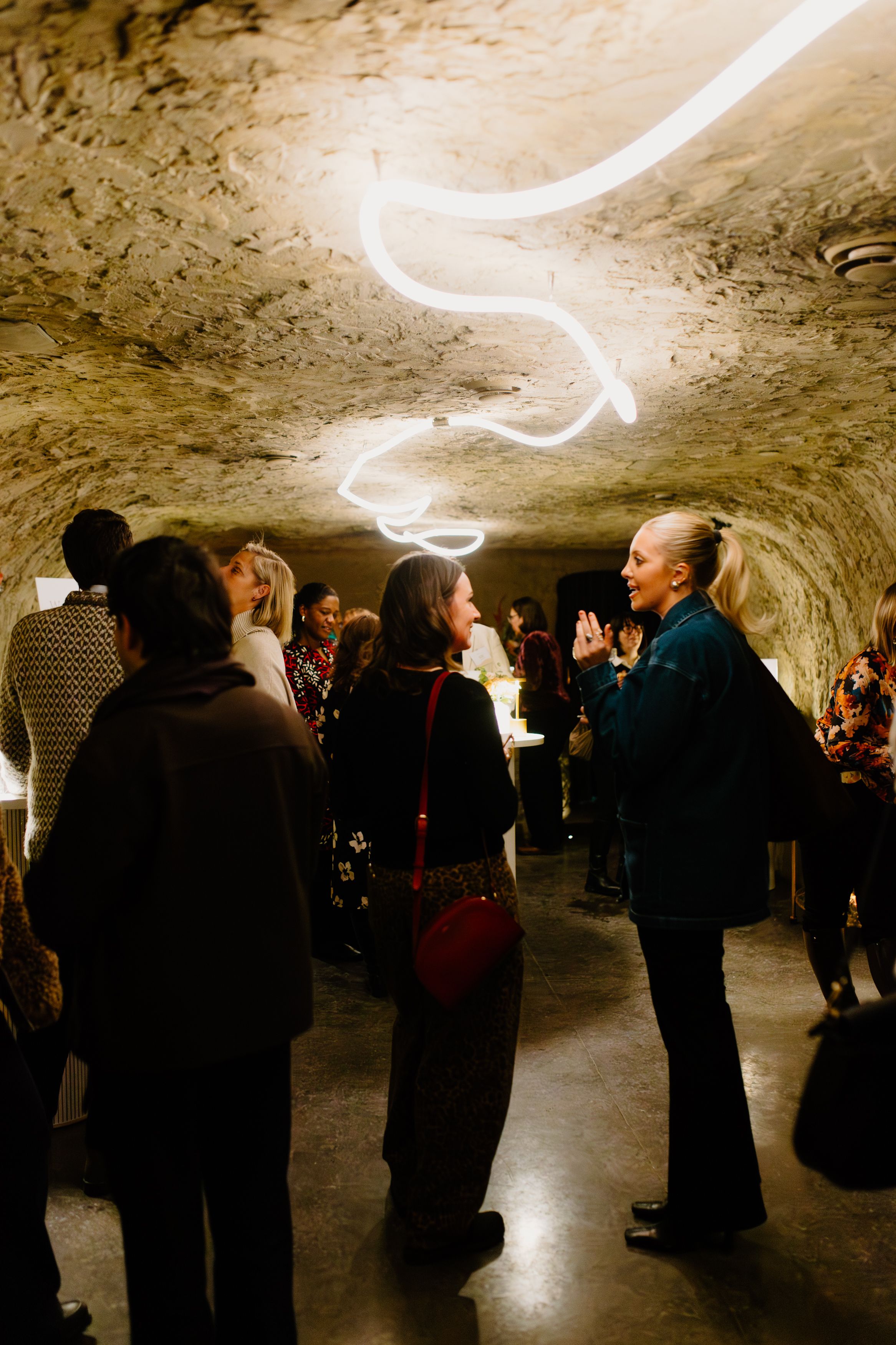 Guests mingling in a dramatic cave venue with glowing neon light installation on stone ceiling.