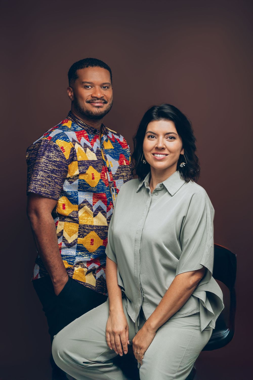 Two people pose together wearing contrasting outfits - one in a vibrant patterned shirt and one in solid light attire.