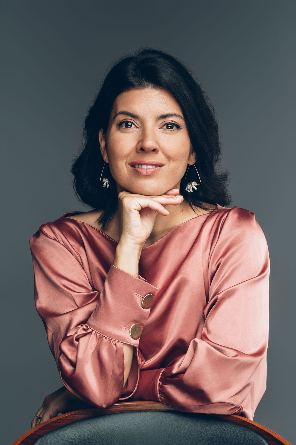 Portrait series showing person in rose-colored satin top posing against gray backdrop wearing gold jewelry.