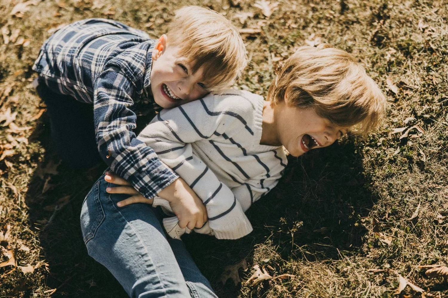 Two young children playing and laughing together on natural ground outdoors.