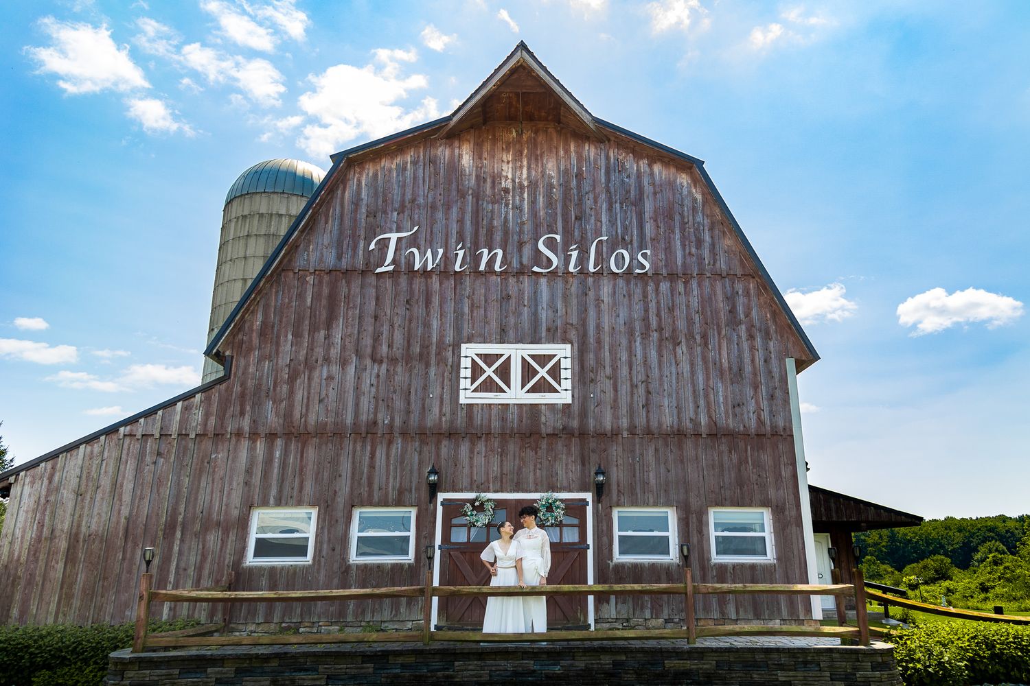 Rustic barn wedding venue with 'Twin Silos' text and couple framed in window.